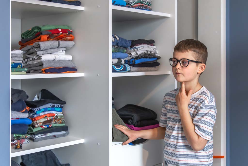 cute boy with glasses stands near wardrobe thinks about what wear